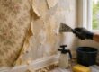 Professional removing stubborn wallpaper and adhesive from a wall in a Massachusetts home